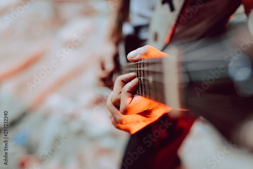 Soft focus of male musician clamping strings on guitar fret board while playing music photo