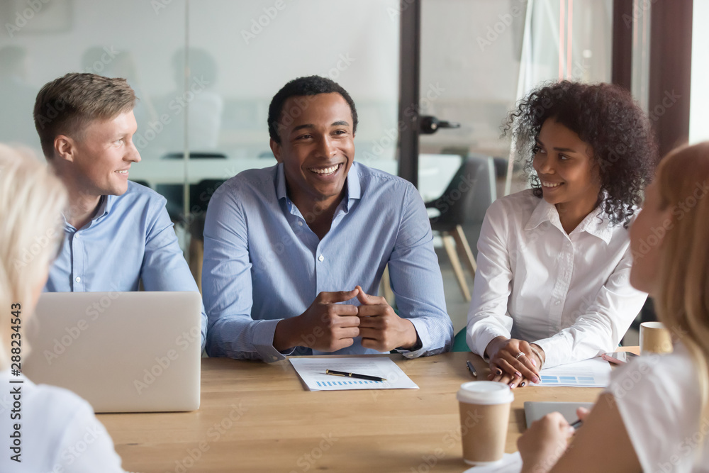 Smiling multiracial colleagues negotiate cooperating at meeting Smiling multiracial colleagues negotiate cooperating at meeting
