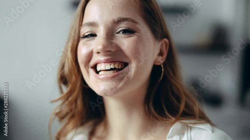 Cheerful good looking young redhead woman with freckles in the apartment looks at camera and smiles sincerely having fun photo