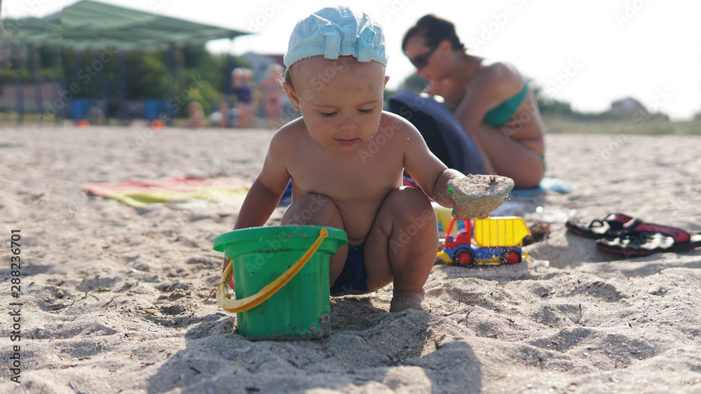 Little boy squatting on sea beach and sculpt a sand construction with pail in his hand Little boy squatting on sea beach and sculpt a sand construction with pail in his hand