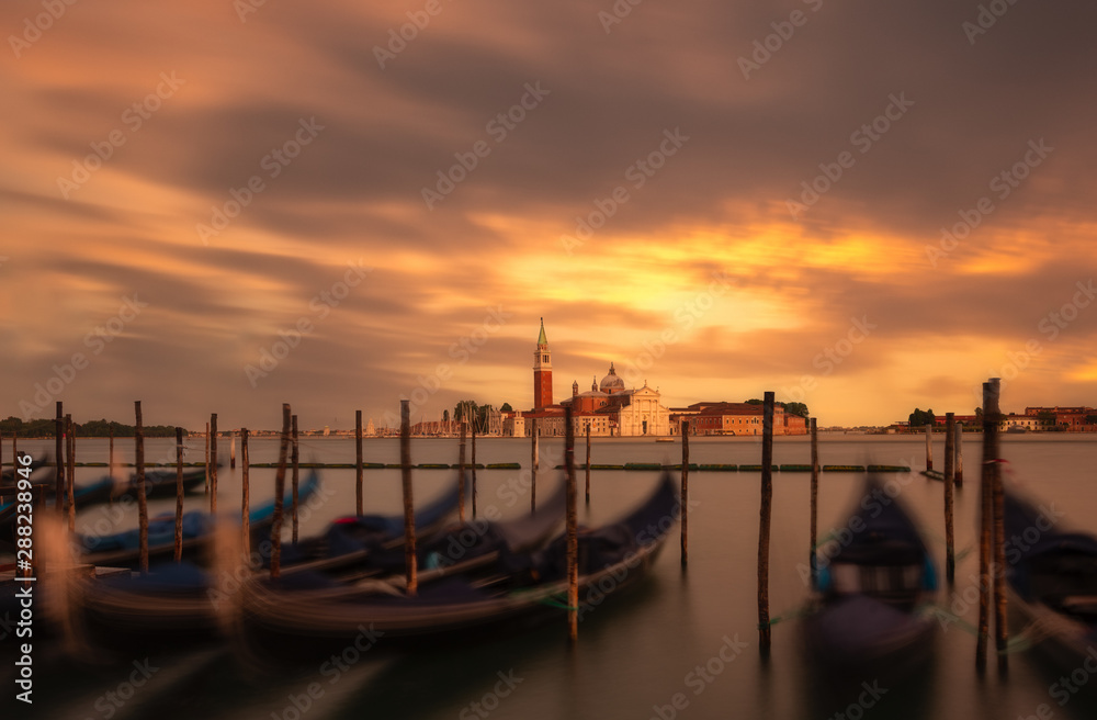 Pier with empty boats in water against fiery sunset and beautiful city with old towers and rooftops