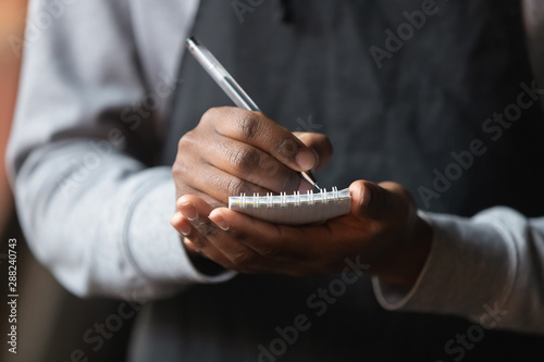 Close up African American waiter hands with notebook, taking customer order photo