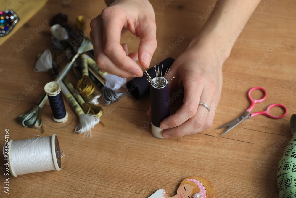 Fototapeta premium woman hands taking out a needle on a wooden table with tools and sewing objects
