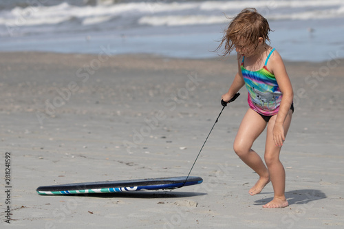 Young girl dragging boogie board in the sand