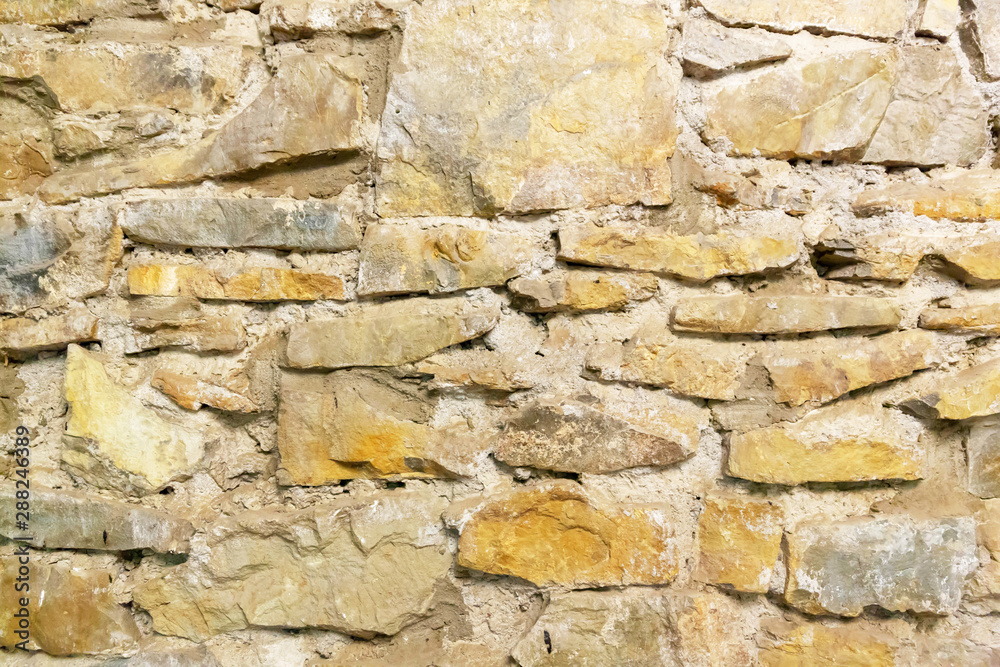A wall of natural stone, sand-colored cement, grey seams. Background image. A wall of natural stone, sand-colored cement, grey seams. Background image.
