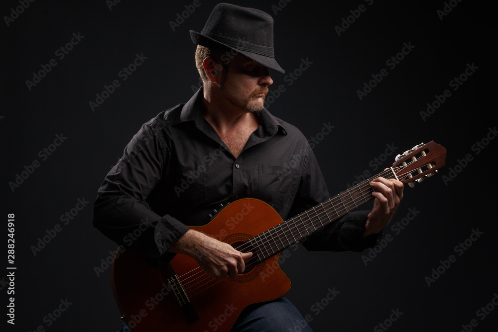 Obraz premium Man in black clothes plays a classic acoustic guitar. Studio photography.