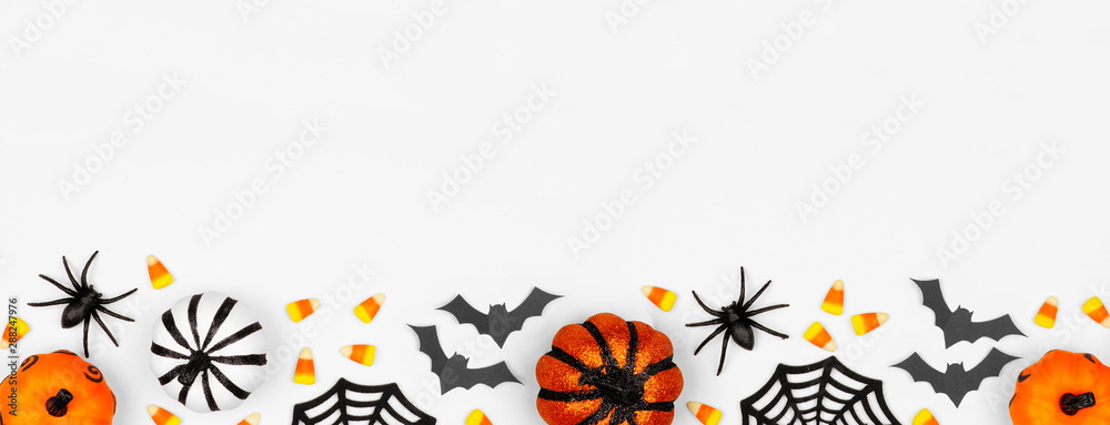 Halloween bottom border banner of pumpkins, candy and decor. Flat lay over a white background with copy space.