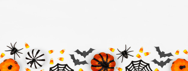 Halloween bottom border banner of pumpkins, candy and decor. Flat lay over a white background with copy space.