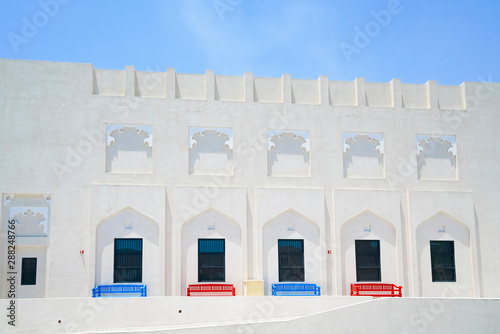 Red and blue bench seats outide white building with Arabic or Islamic design details. photo