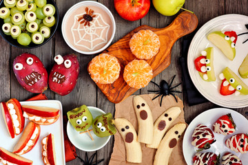 Healthy Halloween fruit snacks. Selection of fun, spooky treats. Top view table scene over a rustic wood background.