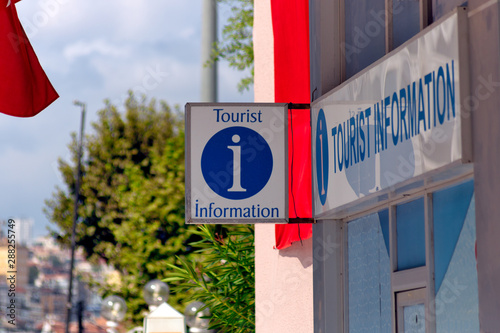 Tourist Information sign with information symbol hanged in front of an information desk. trees and partial sky on the background.