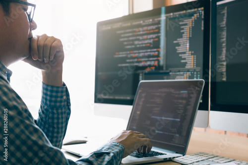 Man programmers are stressed and hand holding nose with headache at the office while working analyzing on desk in code at office room.