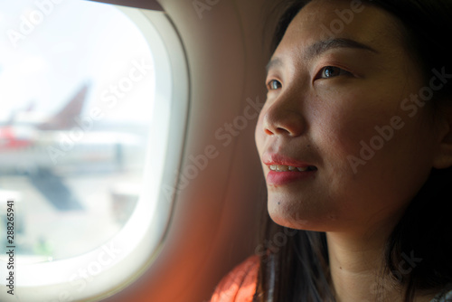 young happy and beautiful Asian Chinese tourist woman smiling excited sitting in airplane by the window arriving destination in aircraft transportation and holidays travel © TheVisualsYouNeed
