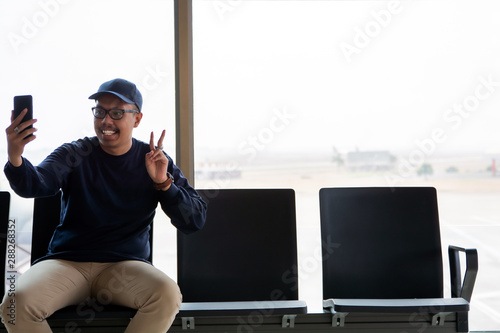Shoot for remember. portrait of delighted young asian man in hat is sitting at airport lounge.