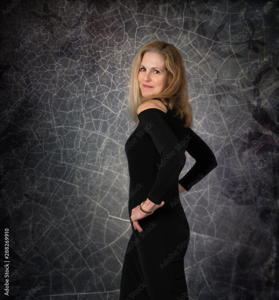 Sexy confident middle aged woman in black dress posing in front of