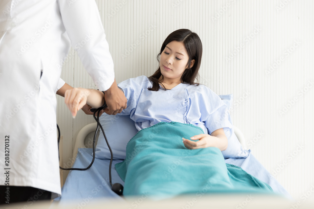 Doctor checking blood pressure of Asian women patient lying in a hospital bed Doctor checking blood pressure of Asian women patient lying in a hospital bed