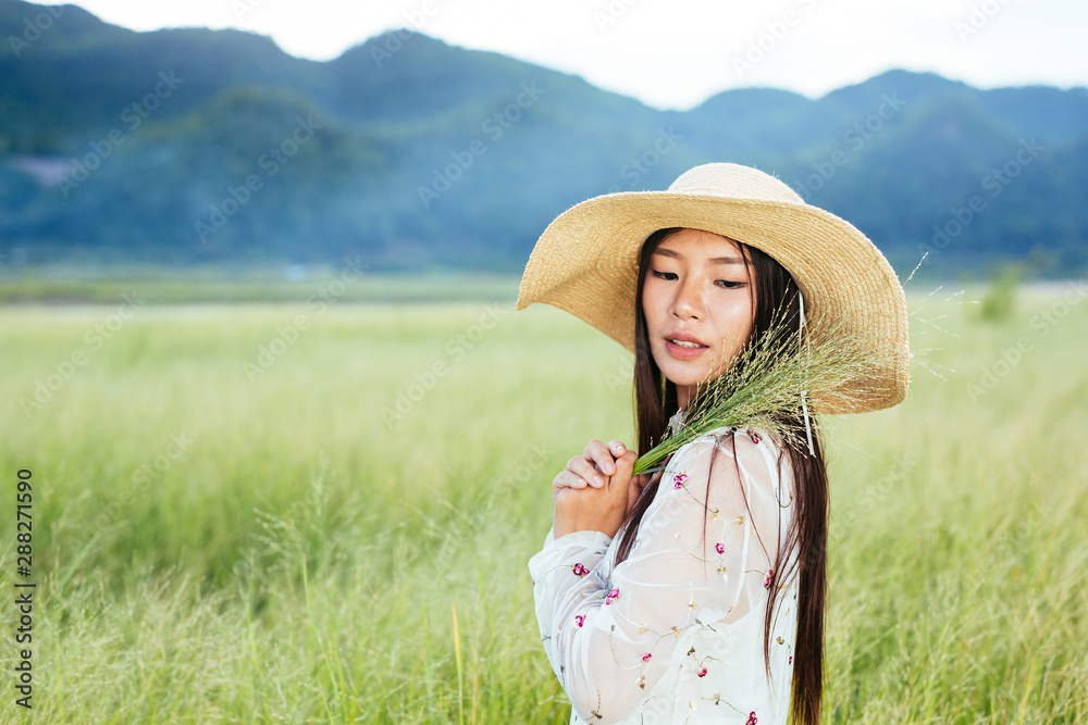 A woman who is holding a grass in her hands on a beautiful grass field with a mountain backdrop.