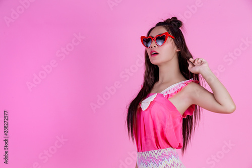 A beautiful woman wearing red glasses with a big hat on a pink background.