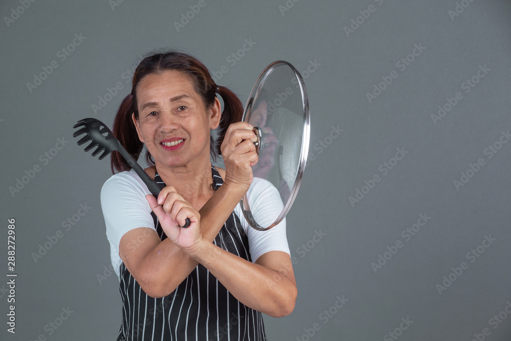 An elderly cook with kitchenware in his hand on a gray background. An elderly cook with kitchenware in his hand on a gray background.