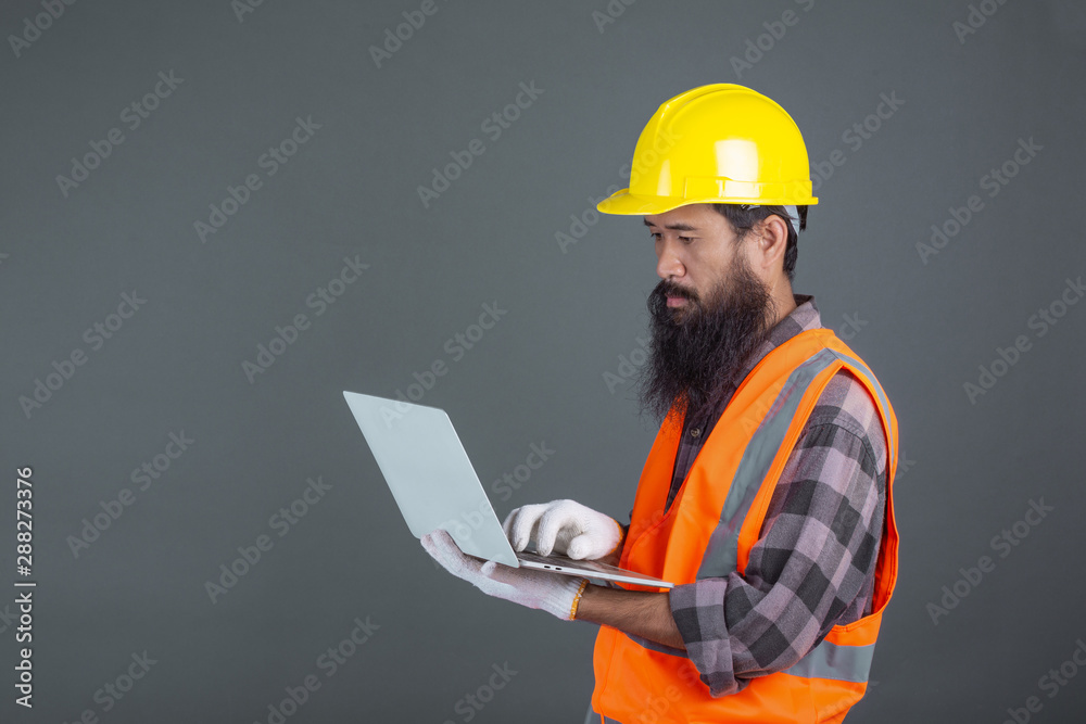 An engineering man wearing a yellow helmet holding a notebook on a gray background. An engineering man wearing a yellow helmet holding a notebook on a gray background.