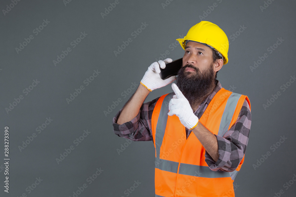 An engineering man wearing a yellow helmet holding a phone on a gray background. An engineering man wearing a yellow helmet holding a phone on a gray background.