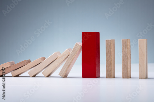 Red Wooden Block Amidst Falling And Upright Domino Pieces