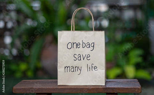 Brown recyclable paper shopping bag Placed on a wooden table, the backdroup is a green tree. For the background image used to campaign, do not use plastic bags. photo