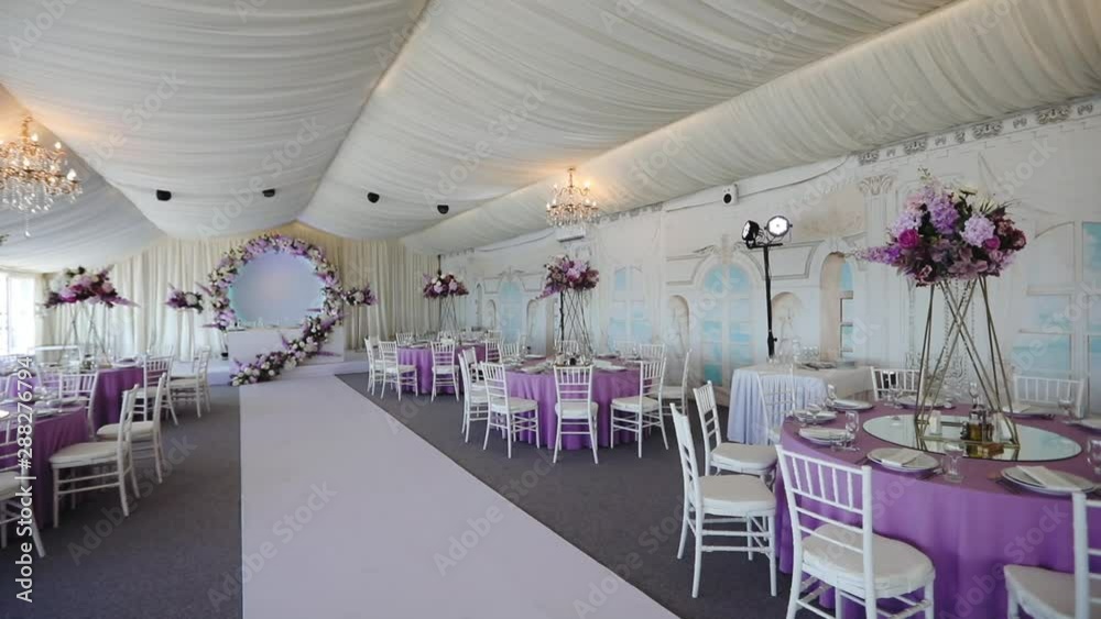 panorama of wonderful empty restaurant hall with purple flowers decoration and white ceiling on wedding day