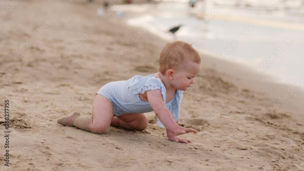 Toddler baby girl crawls the sand towards shallow waterline of Baltic sea beach shore enjoy play in water Toddler baby girl crawls the sand towards shallow waterline of Baltic sea beach shore enjoy play in water