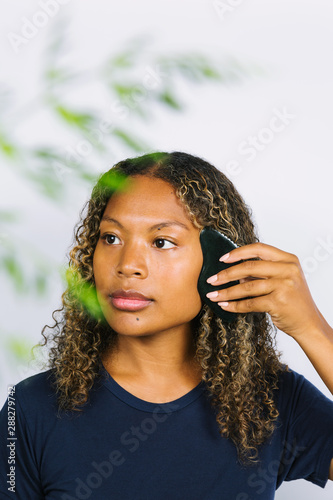 Mixed ethnicity woman using obsidian gua sha stone to massage her face photo