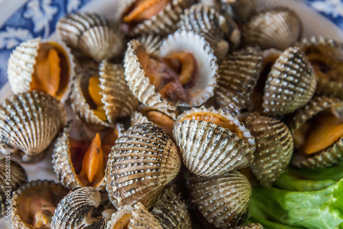 Steamed blanched cockles with Thai seafood dipping sauce and lettuce in the white dish.