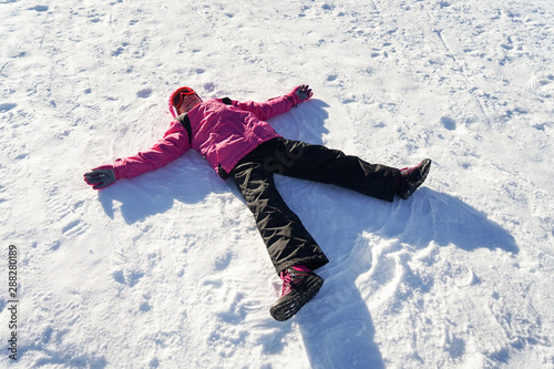 Little girl making a snowangel wearing snow clothes