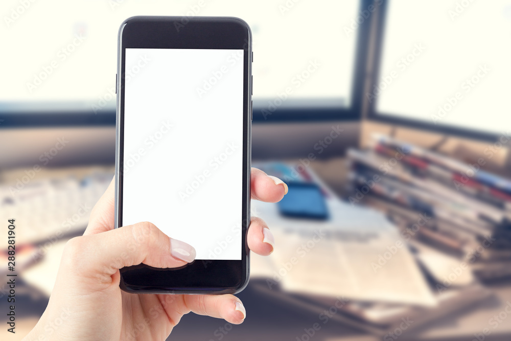 Hand holding a smartphone with a blank screen. Newspapers blurred in the background. Concept of the morning press and telephone in hands.