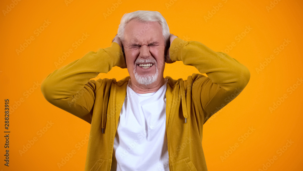 Elderly man closing ears by palms, irritated with gossips, orange background Elderly man closing ears by palms, irritated with gossips, orange background