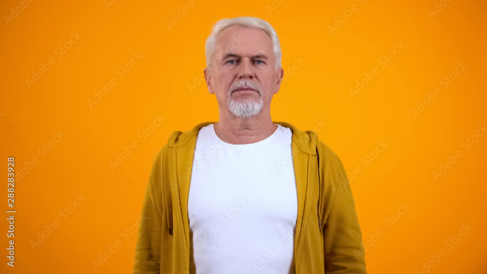 Serious senior man looking at camera, isolated on yellow background, insecurity Serious senior man looking at camera, isolated on yellow background, insecurity
