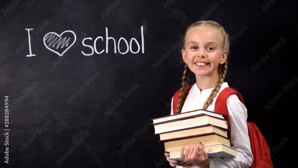 Smiling schoolgirl holding books, I love school written on blackboard, lesson Smiling schoolgirl holding books, I love school written on blackboard, lesson