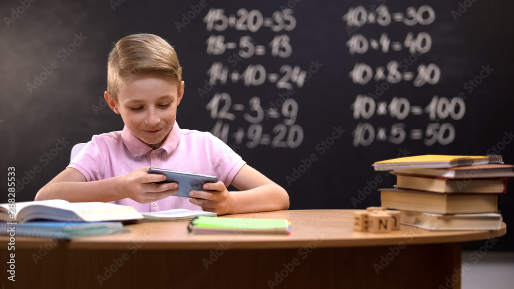 Lazy schoolboy playing videogames on phone instead of preparing task, gadget Lazy schoolboy playing videogames on phone instead of preparing task, gadget