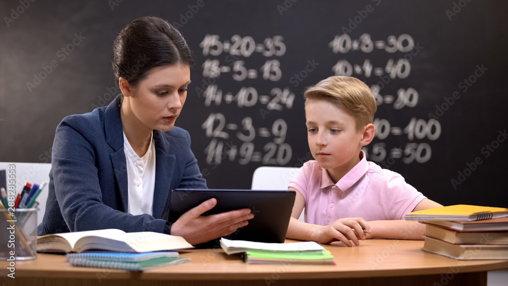 Young teacher showing schoolboy information on tab, private lesson, innovations Young teacher showing schoolboy information on tab, private lesson, innovations
