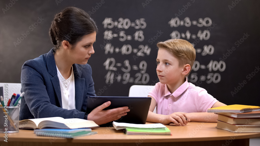 Female teacher explaining schoolboy homework on tab, private lesson, innovations Female teacher explaining schoolboy homework on tab, private lesson, innovations