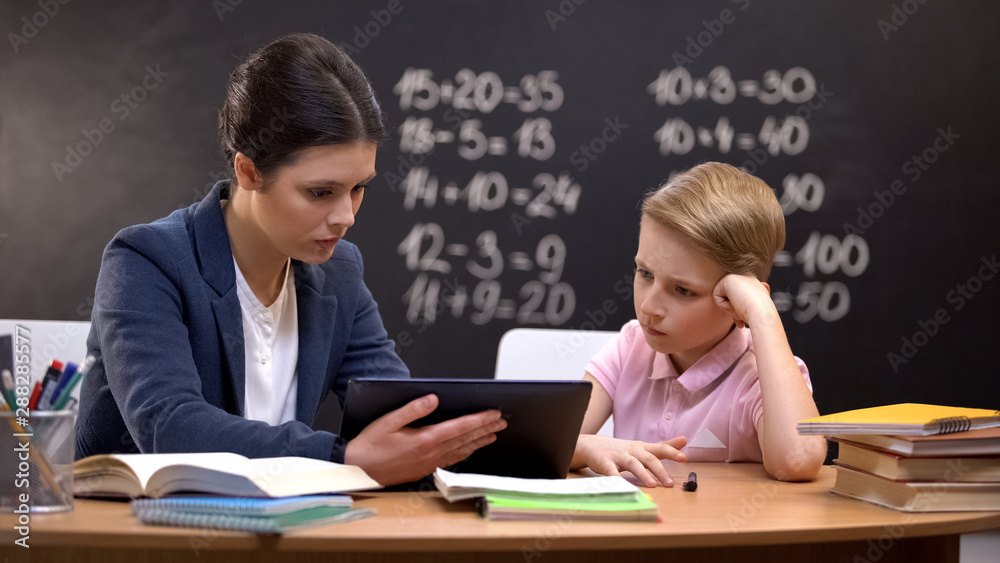 Patient lady teacher explaining subject on tablet, schoolboy does not understand Patient lady teacher explaining subject on tablet, schoolboy does not understand