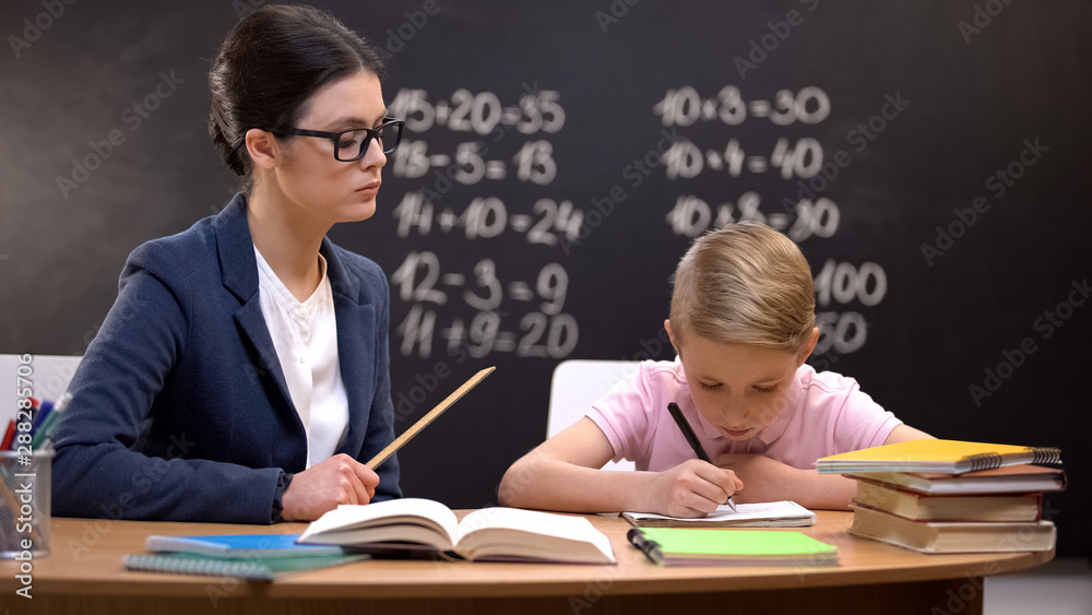 Strict teacher with ruler watching schoolboy doing his homework, control Strict teacher with ruler watching schoolboy doing his homework, control