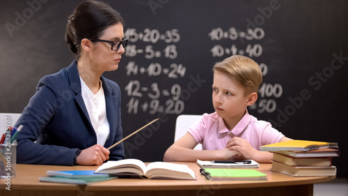 Scared schoolboy cautiously looking at strict teacher with pointer, education