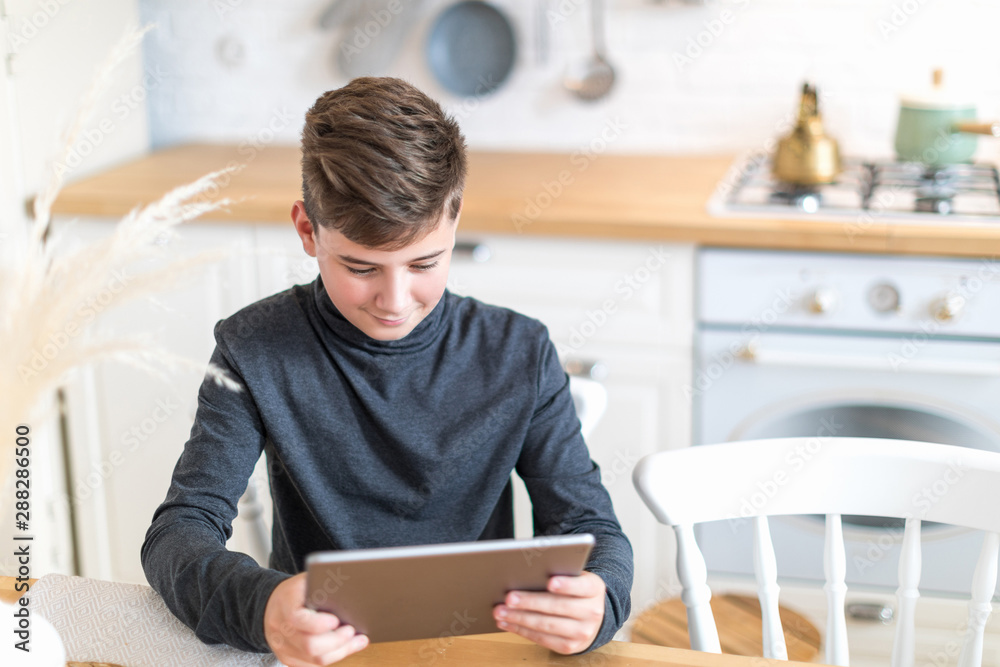 Child in turtleneck sitting at table enjoying game on tablet Child in turtleneck sitting at table enjoying game on tablet