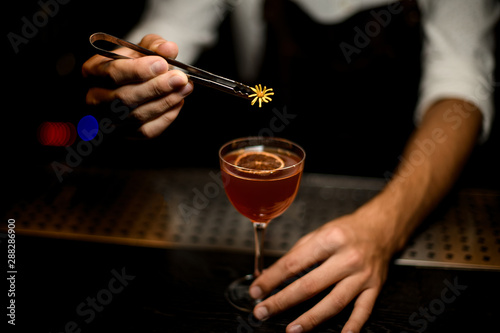 Male bartender serving a cocktail in the glass with a caramelized lemon slice adding a yellow flower