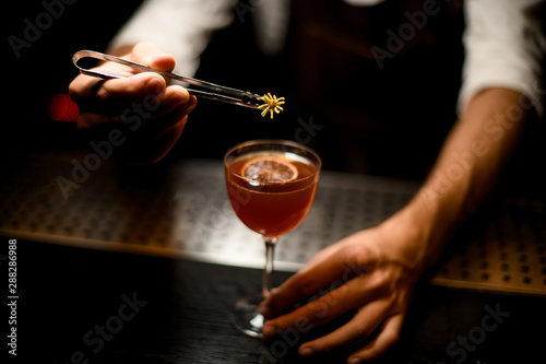 Professional bartender serving a cocktail in the glass with a caramelized lemon slice adding a yellow flower