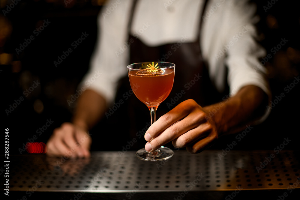 Professional bartender serving a cocktail in the glass with a caramelized lemon slice and a little yellow flower