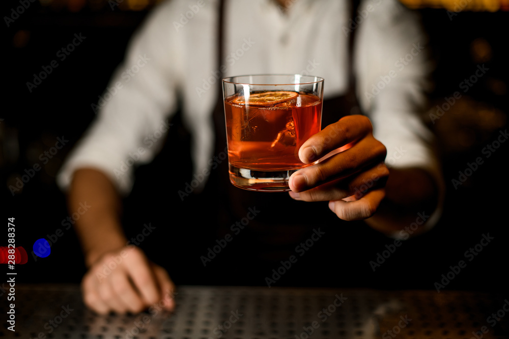 Professional bartender serving a brown orange cocktail decorated with a caramelized lemon slice