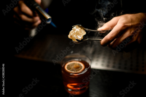 Bartender serving a brown cocktail melting caramel with a burner above the lemon slice