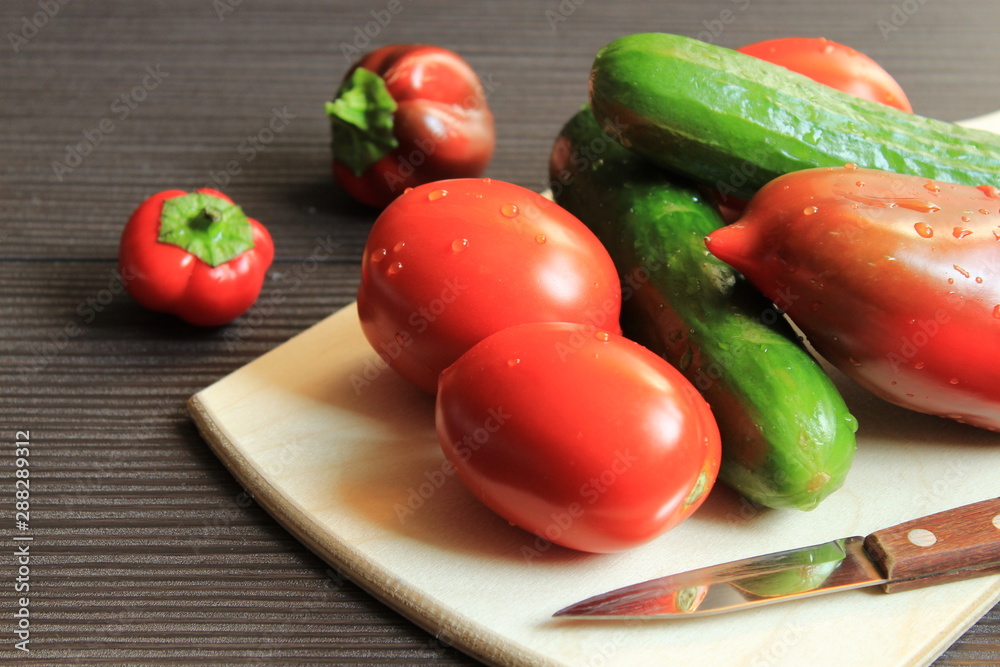 Fresh vegetables with a knife lie on a wooden board. Near the table are two peppers. Fresh vegetables with a knife lie on a wooden board. Near the table are two peppers.