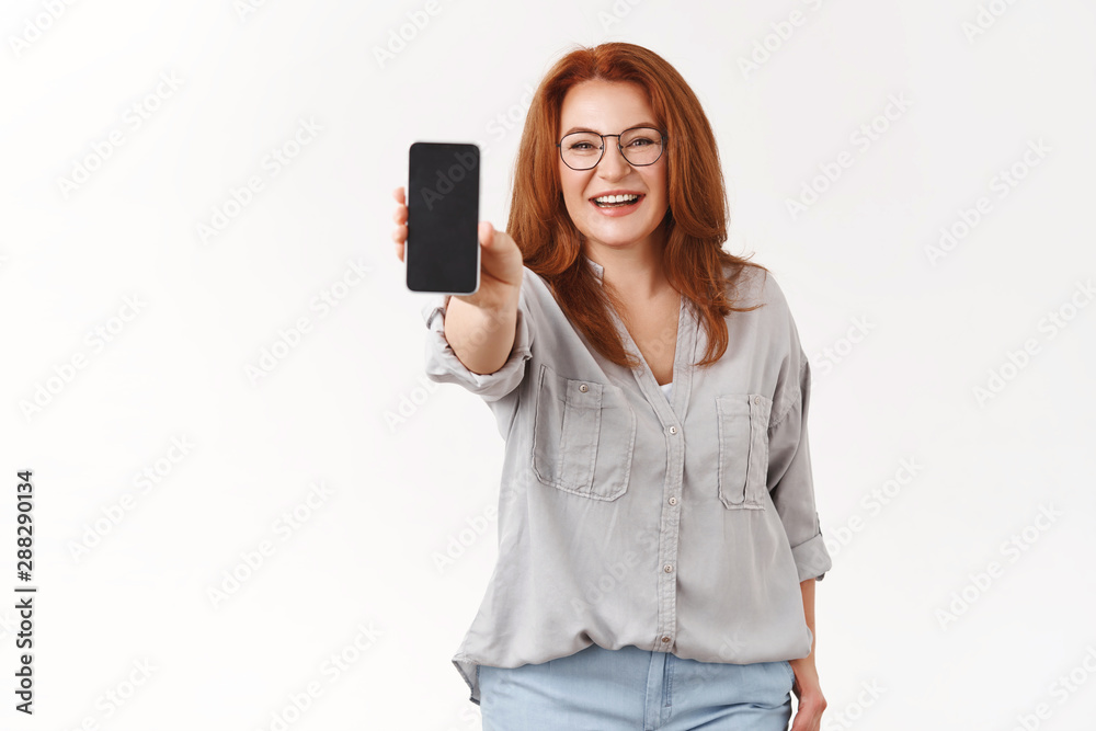 Naklejka premium Woman sharing useful app. Charming elegant redhead middle-aged businesswoman mom wear glasses extend arm hold smartphone show phone screen display promote application white background